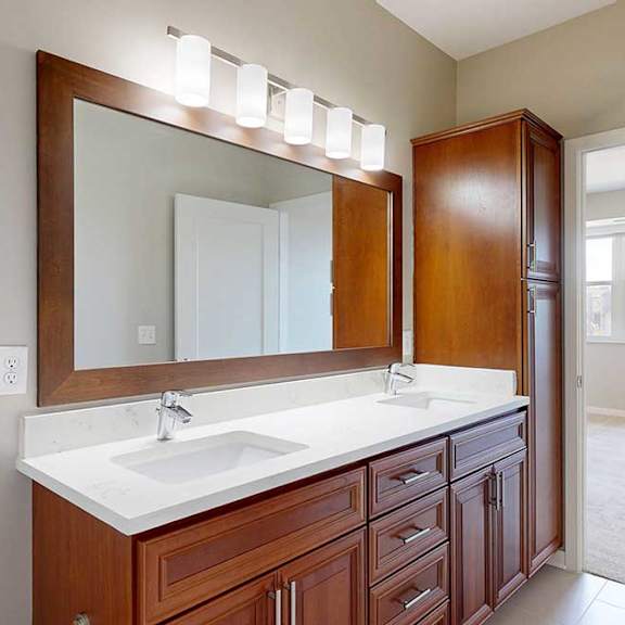 Thumbnail 22 of 27 A bathroom with cherry-stained wooden cabinets, white quartz vanity, a large framed mirror and overhead lighting.
