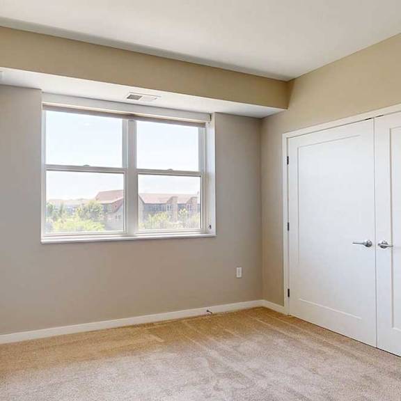 Thumbnail 25 of 27 A carpeted bedroom with a alrge window and a double-door closet.