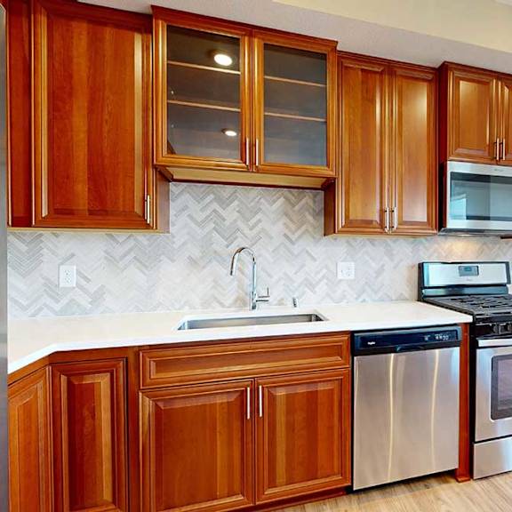 Thumbnail 11 of 27 A kitchen with cherry-stained wooden cabinets, light quartz countertops, and stainless steel appliances.