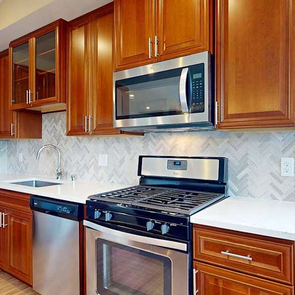 Thumbnail 12 of 27 A close up of a stainless steel range and microwave in a kitchen with cherry-stained wooden cabinets.