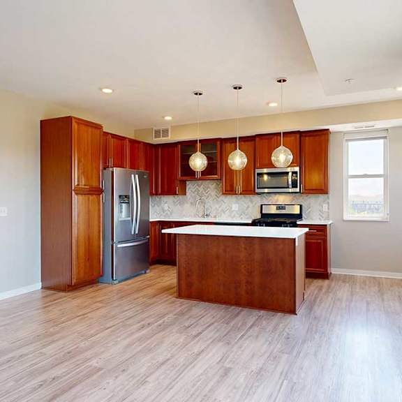 Thumbnail 8 of 27 A kitchen with cherry-stained wooden cabinets, light quartz countertops, stainless steel appliances, and an island with pendant lighting.