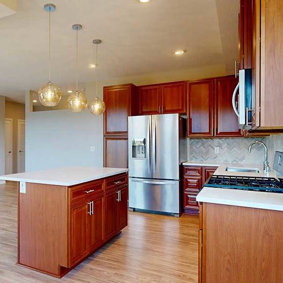 Thumbnail 16 of 27 A kitchen with cherry-stained wooden cabinets, light quartz countertops, stainless steel appliances, and an island with pendant lighting.