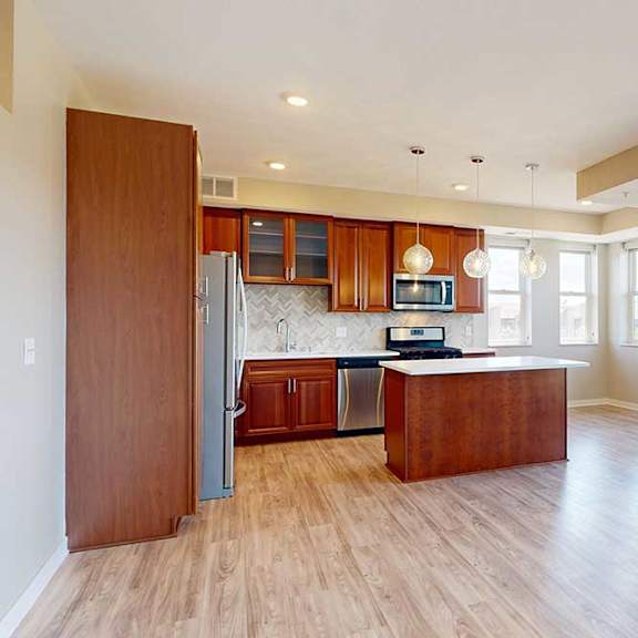 Thumbnail 9 of 27 A living room with hardwood-style flooring, open to a modern kitchen with cherry-stained wooden cabinets.
