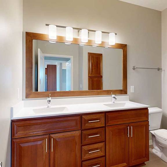 Thumbnail 23 of 29 An attached bathroom with a double-sink vanity with white quartz counters, an oversized mirror, overhead lighting, and a walk-in shower with a glass door.
