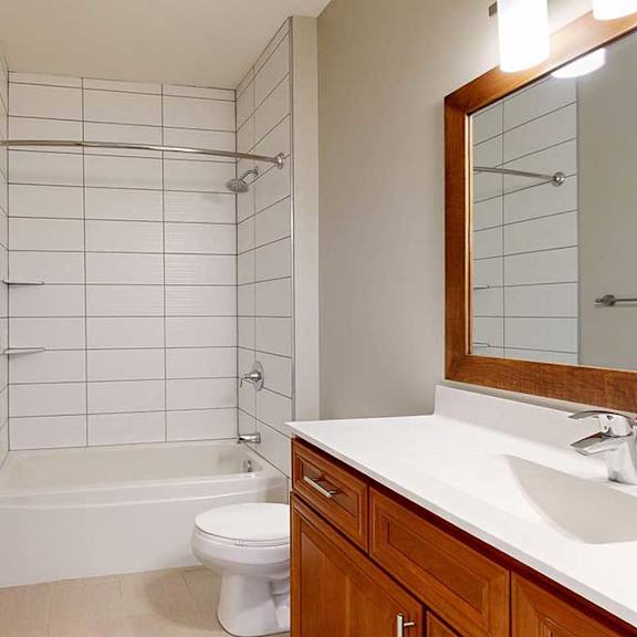 Thumbnail 29 of 29 A hallway bathroom with a cherry-stained vanity sink and a tiled tub shower.