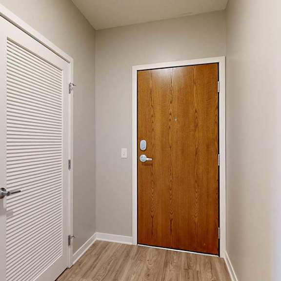 Thumbnail 2 of 29 An entryway with a wooden front door and a white slatted door to a laundry room.