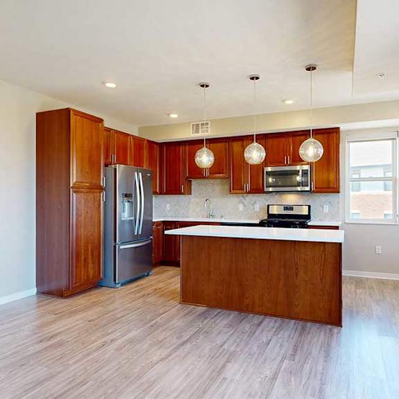 Thumbnail 10 of 29 A kitchen with cherry-stained wooden cabinets, light quartz countertops, stainless steel appliances, and an island with pendant lighting.