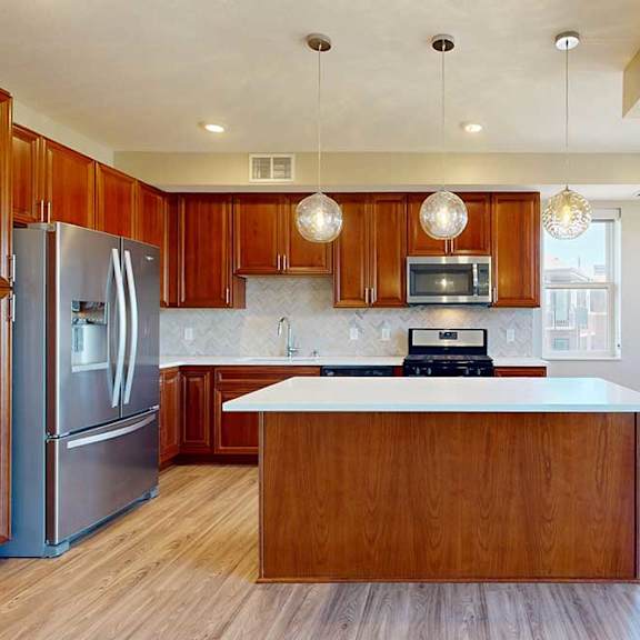 Thumbnail 13 of 29 A kitchen with cherry-stained wooden cabinets, light quartz countertops, stainless steel appliances, and an island with pendant lighting.