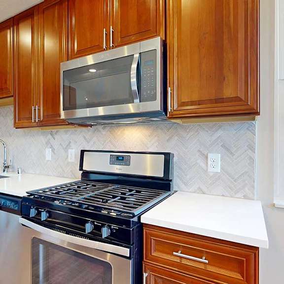 Thumbnail 12 of 29 A close up of a stainless steel range and microwave in a kitchen with cherry-stained wooden cabinets.