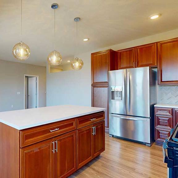 Thumbnail 17 of 29 A kitchen island with cherry-stained wooden cabinets and a light quartz countertop, in front of a spacious living room with a fireplace.