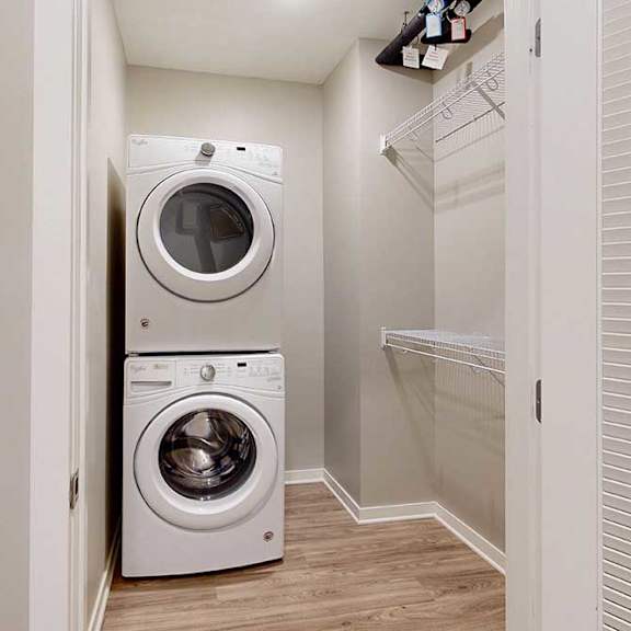 Thumbnail 3 of 29 A laundry room with a stacked washer and dryer, and built-in wire shelves.