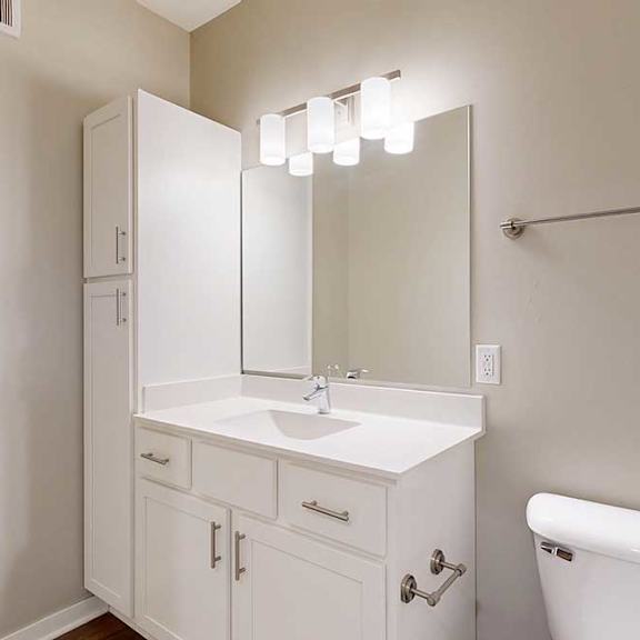 Thumbnail 11 of 13 A bathroom with white cabinets, a white granite vanity, an oversized mirror with overhead lighting, and a tall storage cabinet.