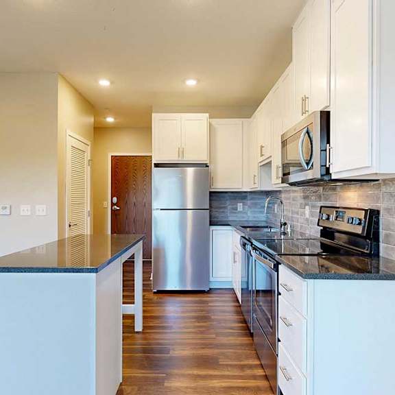 Thumbnail 4 of 13 A modern kitchen with white cabinets, black granite countertops, stainless steel appliances, a tile backsplash, and an island.
