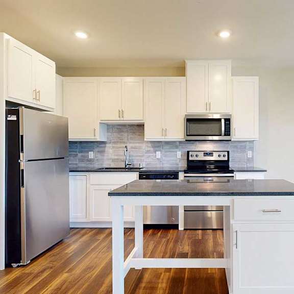 Thumbnail 6 of 13 A modern kitchen with white cabinets, black granite countertops, stainless steel appliances, a tile backsplash, and an island.