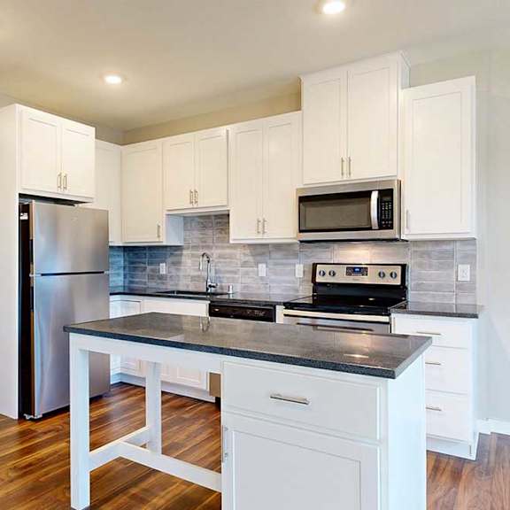 Thumbnail 5 of 13 A modern kitchen with white cabinets, black granite countertops, stainless steel appliances, a tile backsplash, and an island.