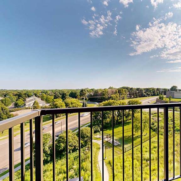 Thumbnail 6 of 27 A balcony overlooks a green landscape with a road and buildings in the distance.