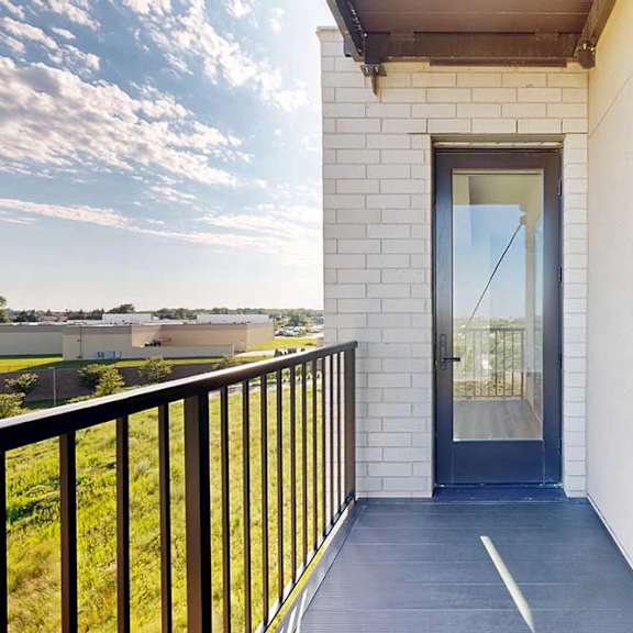 Thumbnail 7 of 27 A balcony with a black railing and a glass door leading to a building.
