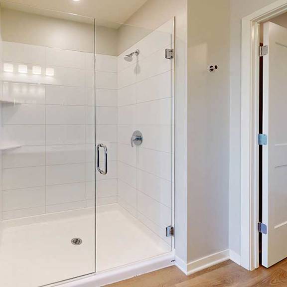 Thumbnail 23 of 27 A white tiled shower with a glass door is in a well-lit bathroom.