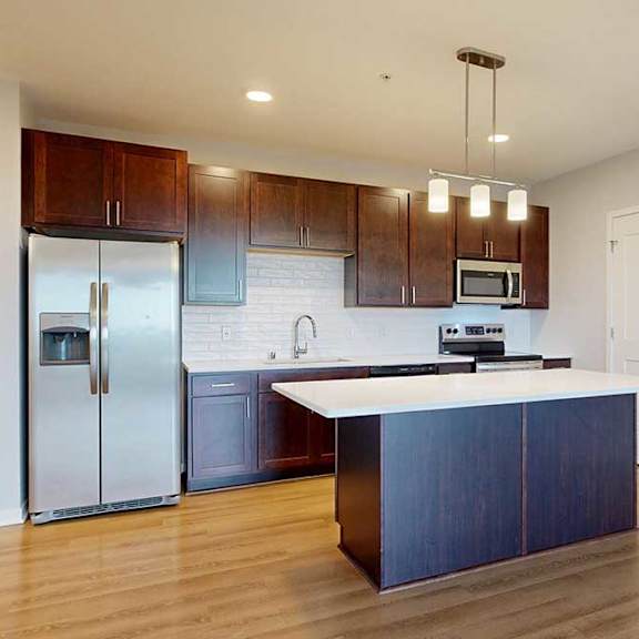 Thumbnail 17 of 27 A kitchen with a white counter top and a refrigerator.