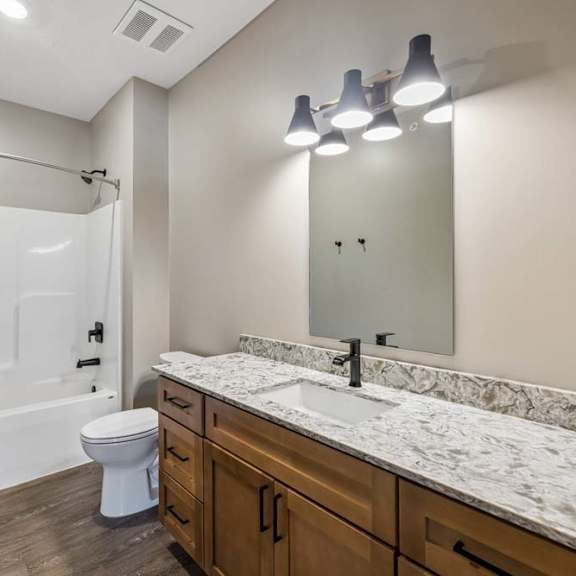 Thumbnail 12 of 17 Bright apartment bathroom with a double-sink vanity, stone-look countertop, large mirror, and tub-shower combination.