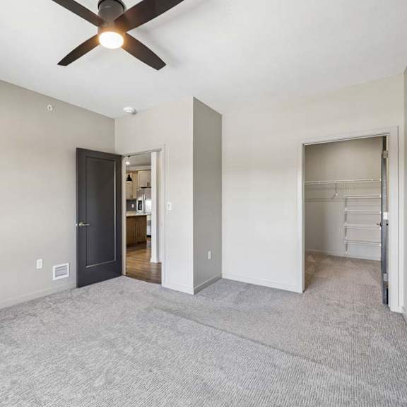 Thumbnail 14 of 17 Spacious bedroom with neutral carpet, ceiling fan, and an open doorway leading toward the walk-in closet and adjoining areas.