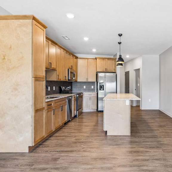 Thumbnail 9 of 17 Open-concept apartment kitchen with wood cabinetry, a center island, pendant lighting, and sightlines into the living area.