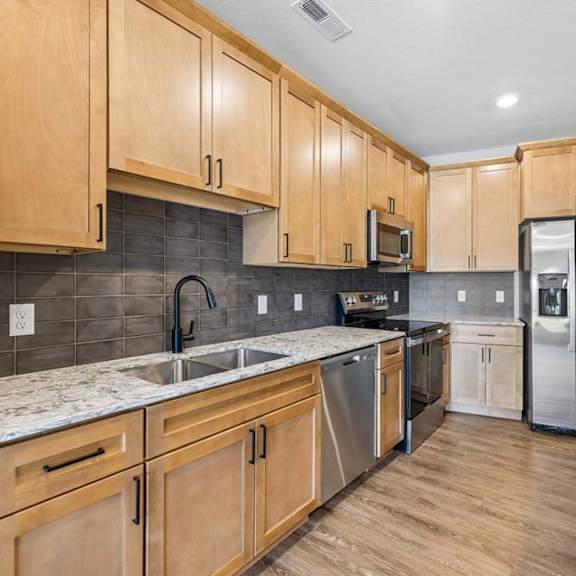 Thumbnail 3 of 17 Modern kitchen featuring wood cabinets,quartz countertops, stainless steel appliances, and ample counter space for meal preparation.