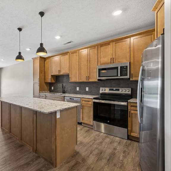 Thumbnail 2 of 17 Spacious kitchen and living area featuring a large island, stainless steel appliances, wood cabinets, and abundant natural light from oversized windows.