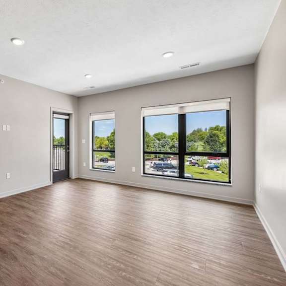 Thumbnail 6 of 17 Spacious apartment living room with large windows, wood-look flooring, and views of the surrounding community.