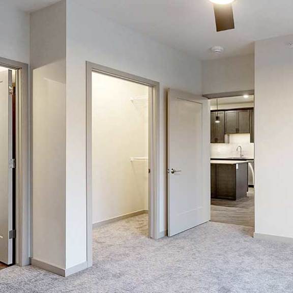 Thumbnail 24 of 29 a bedroom with carpeted flooring, a door to the living room, a large window, a ceiling fan, and an L-shaped walk-in closet
