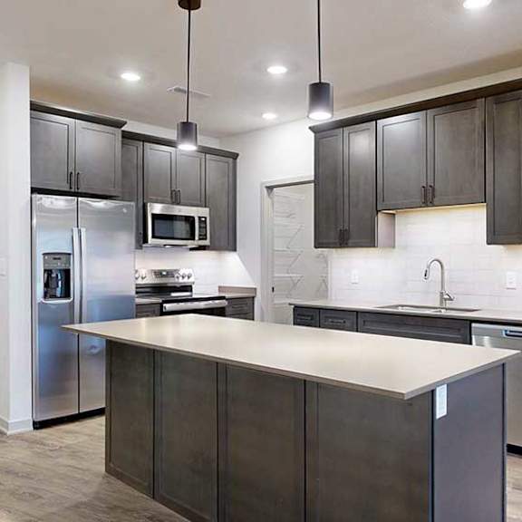 Thumbnail 8 of 29 a modern kitchen with dark wood cabinets, quartz countertops, stainless steel appliances, and a large central island