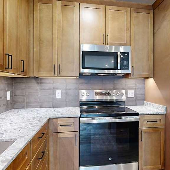 Thumbnail 6 of 29 a kitchen with light brown wooden cabinets, quartz countertops, a grey tile backsplash, and stainless steel appliances