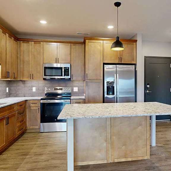Thumbnail 5 of 29 a kitchen with a large table island, light brown wooden cabinets, quartz countertops, and stainless steel appliances