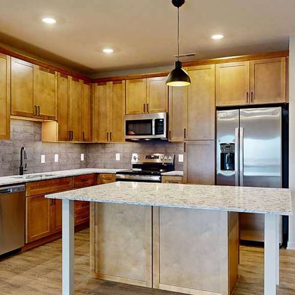 Thumbnail 29 of 29 a kitchen with a large table island, light brown wooden cabinets, quartz countertops, and stainless steel appliances