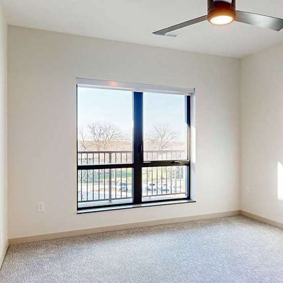 Thumbnail 18 of 28 a bedroom with carpeted flooring, a ceiling fan, and a large window looking out to a balcony
