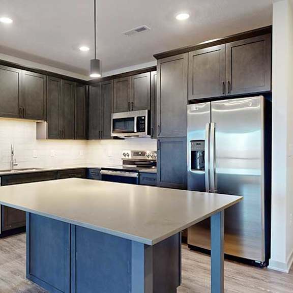 Thumbnail 4 of 28 a modern kitchen with dark wood cabinets, light quartz countertops, a tile backsplash, a large central island, and stainless steel appliances