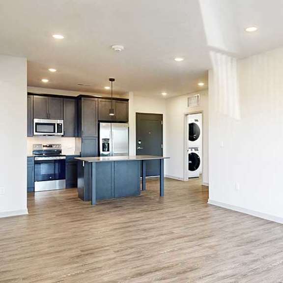 Thumbnail 12 of 28 a living room with hardwood flooring next to a kitchen with dark cabinets and a large central island