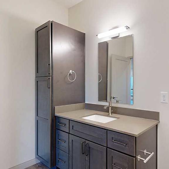Thumbnail 22 of 24 A bathroom with dark wooden cabinets, a quartz vanity sink, mirror with overhead lighting, and a tall storage cabinet.