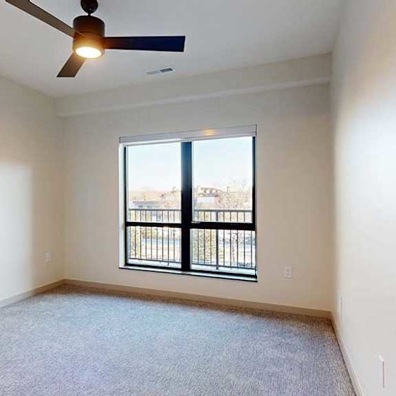 Thumbnail 19 of 24 A bedroom with a large floor-to-ceiling window, a ceiling fan, and carpeted flooring.