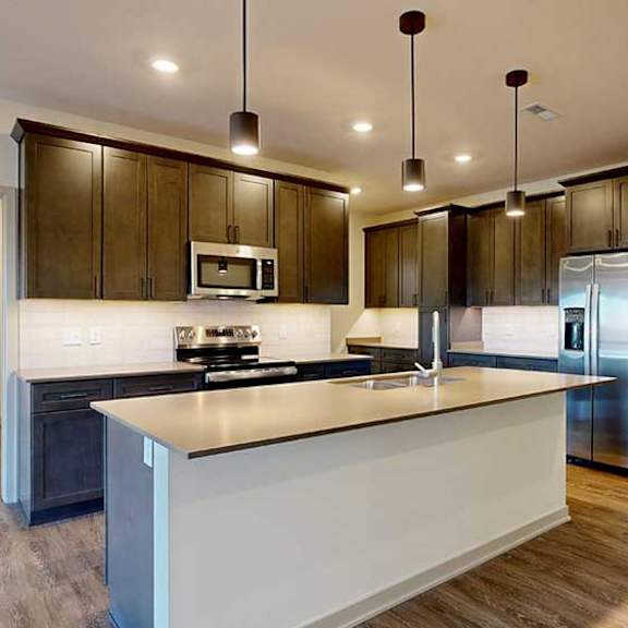 Thumbnail 3 of 24 A kitchen with dark wooden cabinets, quartz countertops, an island, and stainless steel appliances.