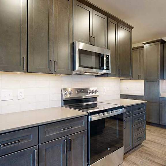 Thumbnail 6 of 24 A close up of the stainless steel microwave and range in a kitchen with dark wooden cabinets.