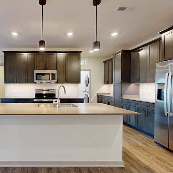 Thumbnail 8 of 24 A kitchen with dark wooden cabinets, quartz countertops, an island, and stainless steel appliances.