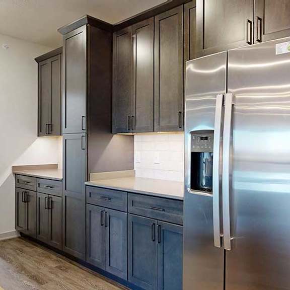 Thumbnail 4 of 24 A kitchen with dark wooden cabinets, quartz countertops, an island, and stainless steel appliances.