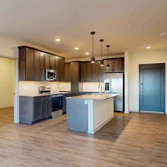 Thumbnail 15 of 24 A living room with hardwood-style flooring and kitchen with dark wooden cabinets.