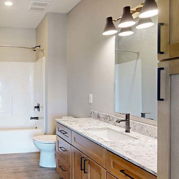 Thumbnail 41 of 42 Modern apartment bathroom with a single-sink vanity, wood cabinetry, stone-look countertop, large mirror, bathtub and shower combination, and neutral finishes.