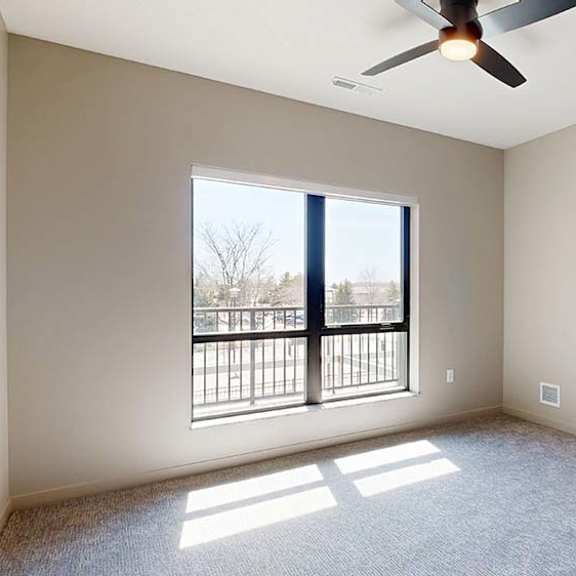 Thumbnail 37 of 42 Bright apartment bedroom with soft carpeting, a large window providing natural light, ceiling fan, neutral finishes, and an open doorway leading to an adjoining room.