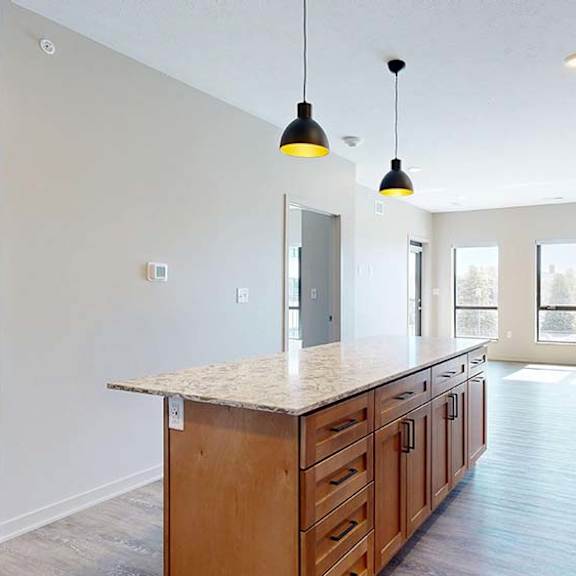 Thumbnail 33 of 42 Spacious apartment kitchen with a large island, wood cabinetry, stainless steel appliances, pendant lighting, stone-look countertops, and an open layout flowing into the bright living area.