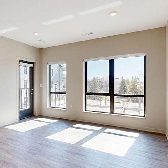 Thumbnail 34 of 42 Bright open-concept apartment living area with wood-style flooring, large windows, abundant natural light, and a glass door leading to a private balcony.