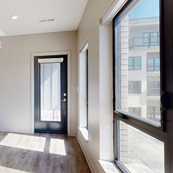 Thumbnail 35 of 42 Bright open-concept apartment living area with wood-style flooring, large windows, abundant natural light, and a glass door leading to a private balcony.
