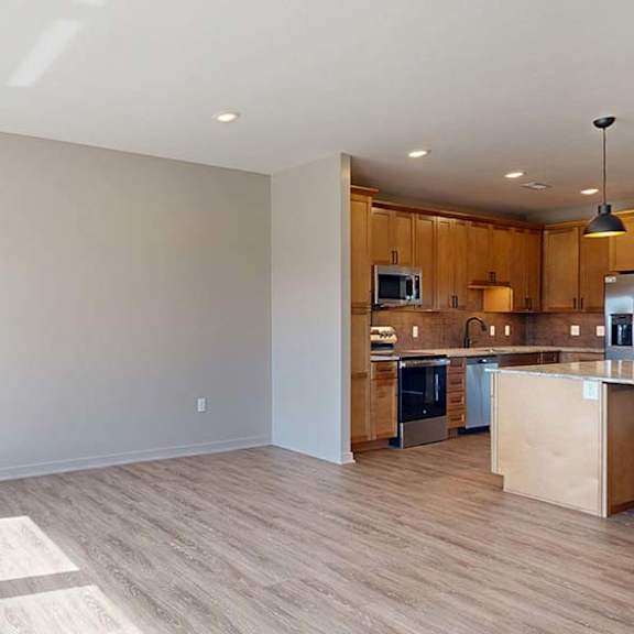 Thumbnail 30 of 42 Bright open-concept apartment living room and kitchen with wood-style flooring, large windows, natural light, wood cabinetry, a kitchen island, and stainless steel appliances.